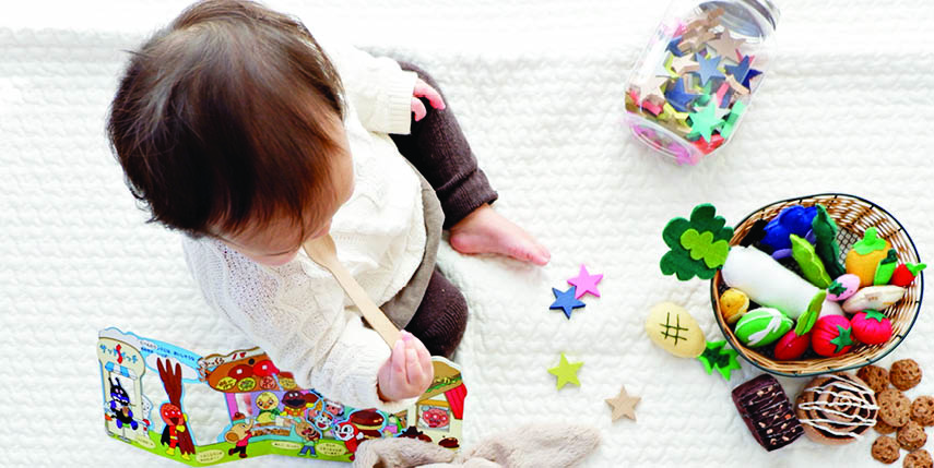 Baby mit Spielzeug auf weisser Decke